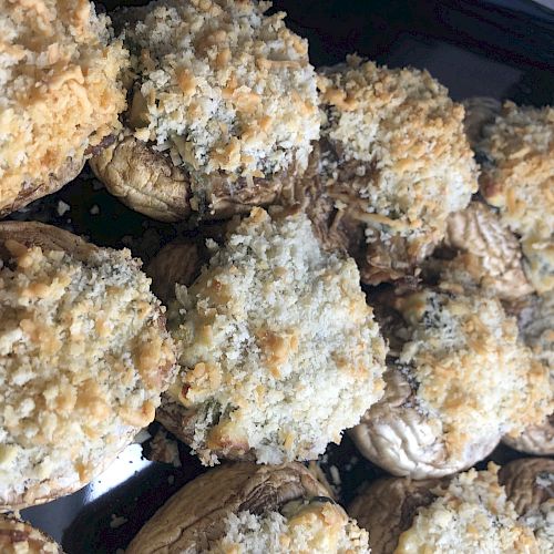 A close-up image of stuffed mushrooms topped with a breadcrumb and cheese mixture, arranged on a black tray.