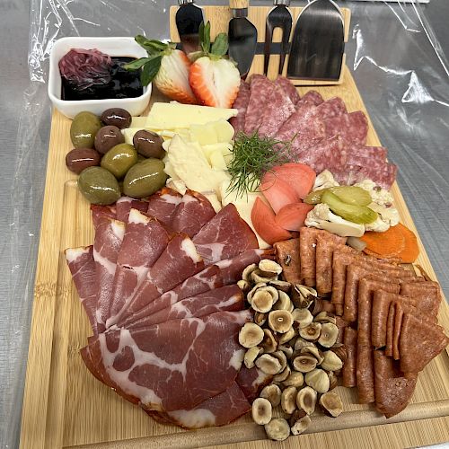 This image shows a charcuterie board with various cured meats, cheeses, olives, nuts, strawberries, pickles, and a dip.