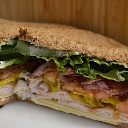 A sandwich with turkey, lettuce, tomato, red onion, pickles, and cheese on whole wheat bread against a wooden background.