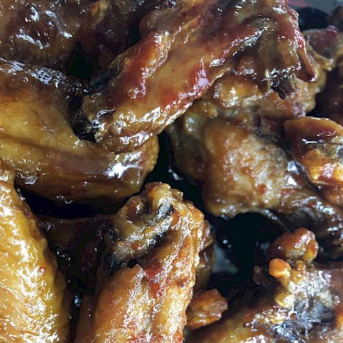 The image shows a close-up of several glazed, cooked chicken wings, showcasing their crispy texture and golden-brown color.