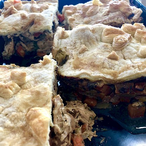 The image shows a close-up of a savory pie cut into four pieces. The pie has a golden, flaky crust with a filling of vegetables and possibly meat.