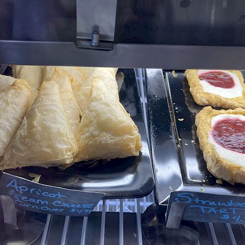 The image shows a display case with apricot cream cheese turnovers on the left and strawberry tarts priced at $4 each on the right.