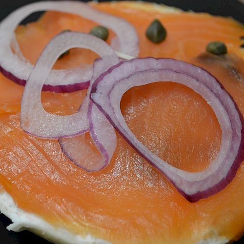 The image shows a bagel with cream cheese, smoked salmon, red onion rings, and capers on top. This is a classic presentation often enjoyed for breakfast.