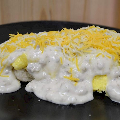 The image shows a dish consisting of scrambled eggs, gravy, and shredded cheese on a plate. The dish is served on a black plate, ending the sentence.