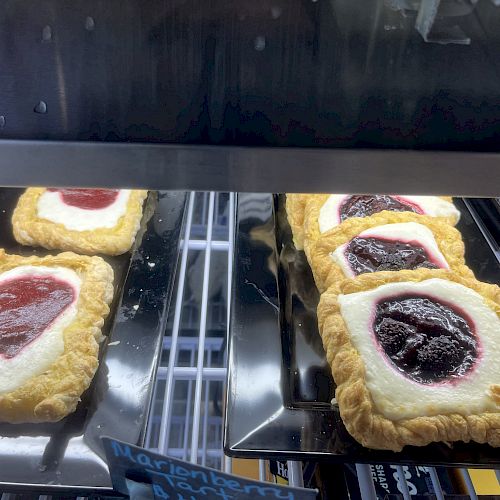 This image shows a display case with rectangular pastries, each topped with a dollop of fruit jam and cream filling. A label reads 