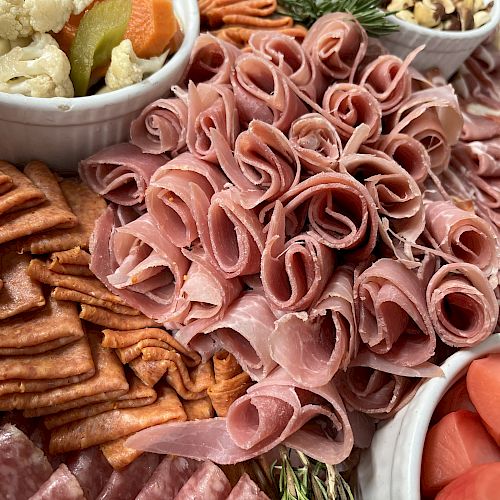 This image shows a charcuterie board with various meats, crackers, pickled vegetables, nuts, and garnished with some herbs.