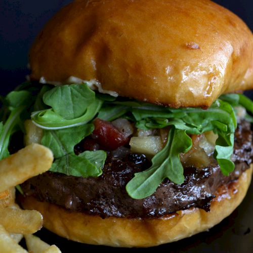 A hamburger with arugula and toppings, served with fries on the side.