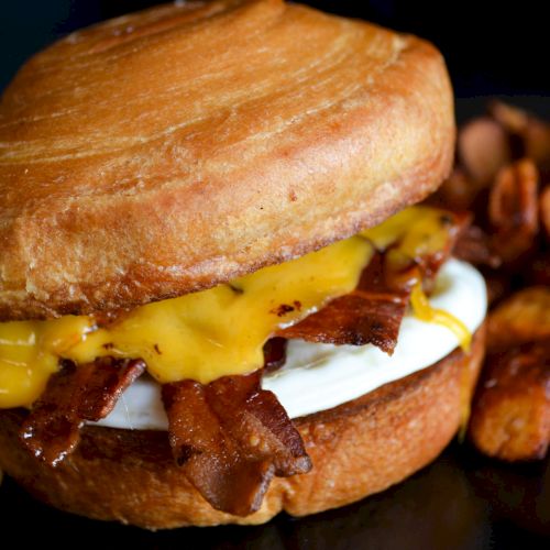 A sandwich with bacon, egg, and cheese, served alongside crispy potato wedges.