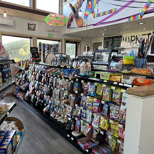 This image shows the interior of a small store with shelves stocked with various products. Bright decorations hang from the ceiling.