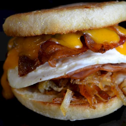 The image shows a sandwich with bacon, egg, cheese, ham, and hash browns on an English muffin.