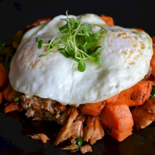 A dish with an egg over roasted vegetables and greens.
