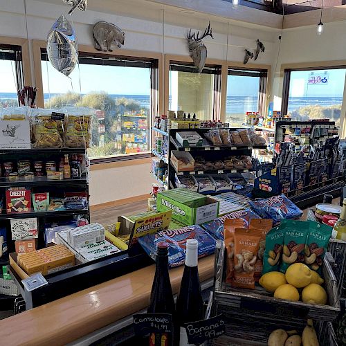 A small store with snacks, beverages, and household items, set against a backdrop of large windows providing a scenic ocean view, ending the sentence.