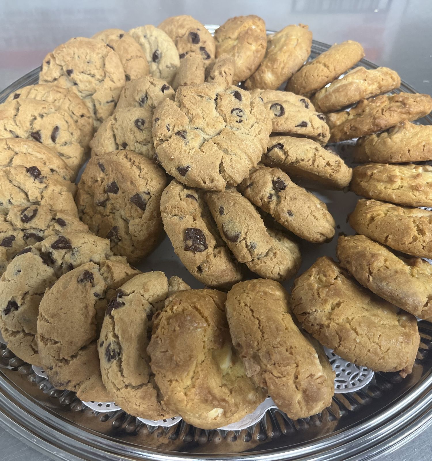 A silver platter is filled with an assortment of chocolate chip cookies arranged in a circular pattern, ready to be served.