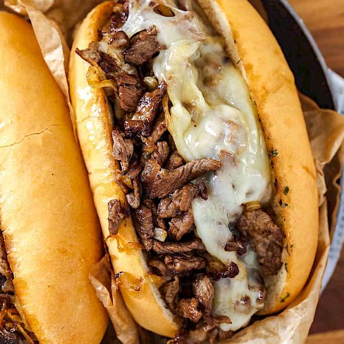 This image shows a cheesesteak sandwich topped with melted cheese and thinly sliced beef on a hoagie roll placed on crumpled parchment paper.