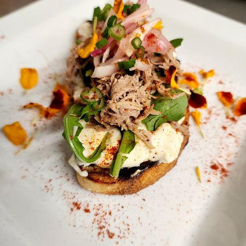 An open-faced sandwich with shredded meat, avocado, sliced radishes, and green onions on a toasted slice of bread, garnished with paprika.