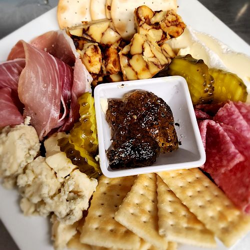 A charcuterie board with meats, crackers, pickles, cheeses, and a small dish of chutney or jam in the center.