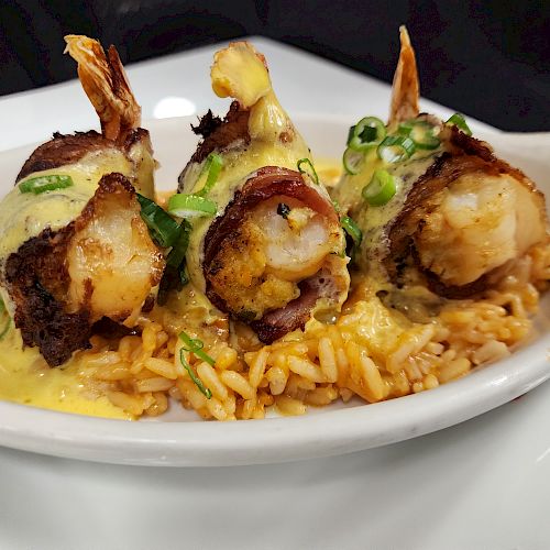 The image shows bacon-wrapped shrimp served on a bed of seasoned rice, garnished with green onions and covered in a creamy sauce.